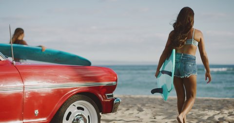 Young attractive women at the beach with vintage beach cruiser car, getting ready to surf at sunset, island beach lifestyle