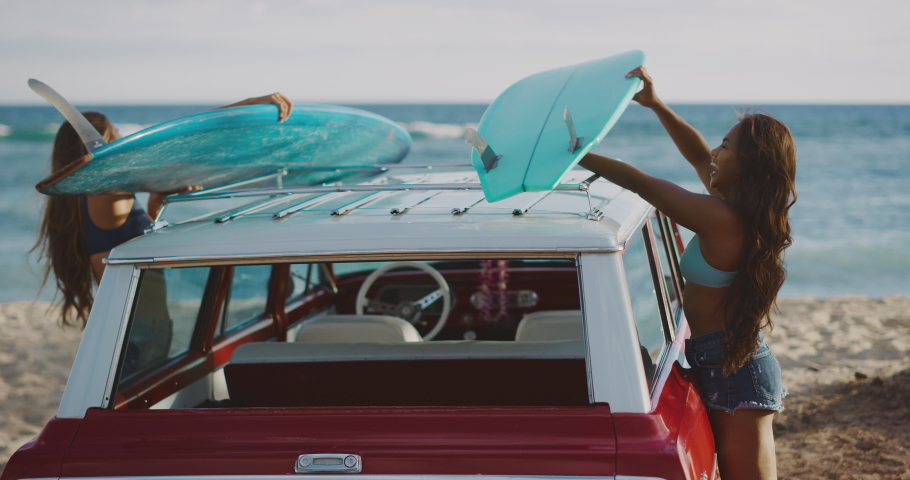 Young attractive women at the beach with vintage beach cruiser car, getting ready to surf at sunset, island beach lifestyle