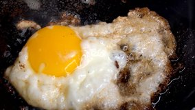 This close up macro video shows a spatula flipping a fresh, sizzling fried egg over in a cast iron pan.
