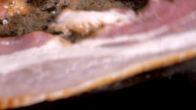 This close up macro video shows delicious fresh bacon cooking and sizzling in a cast iron pan.