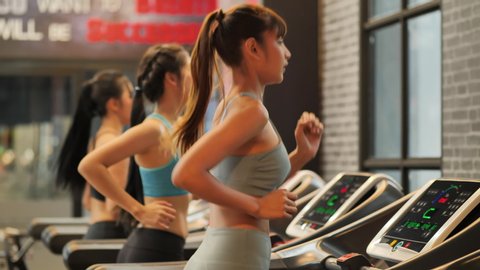 Group Young beautiful woman asian running on a treadmill at gym. Fitness and healthy lifestyle concept. Side view of girl in sportswear jogging exercise. Slow motion