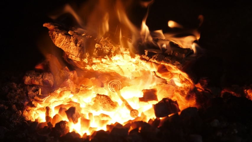  Magic view of a wrought metallic rod kept in tongs and put in a shiny forge full of ravaging blaze with orange and red tongues of flame.