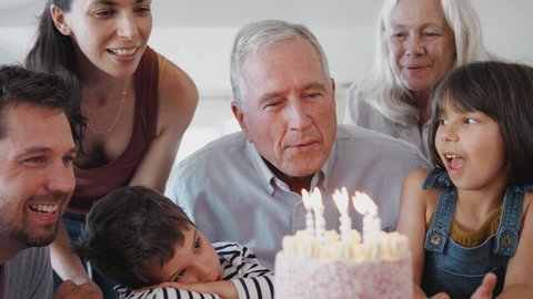 Multi Generation Family Celebrating Birthday With Grandfather At Home As She Blows Out Candles