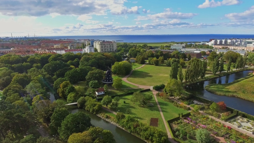 Birds view of going towards an old windmill over the garden in slottsparken, Malmoe, Sweden with oresund in the background in 4k.