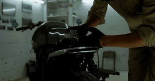 Caucasian male mechanic wearing overalls building custom motorcycle, grinding motorcycle body in his garage. 4K UHD RAW edited footage