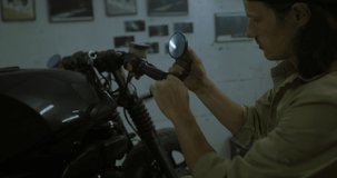 Caucasian male mechanic wearing overalls building custom vintage motorcycle in his garage. 4K UHD RAW edited footage