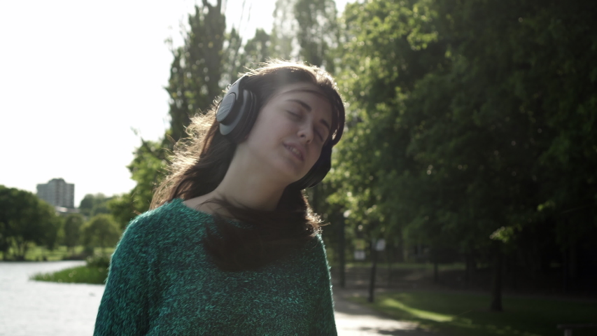 Attractive young Italian woman with headphones listening to music at the park with a sunset look around smile, dancing, enjoying life. portrait close up slow motion