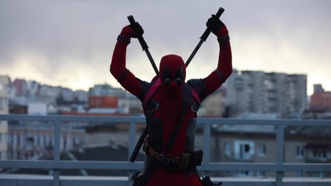 DNIPRO, UKRAINE - MARCH 28, 2019: Deadpool cosplayer posing with guns and katanas behind his back against the background of the urban landscape.
