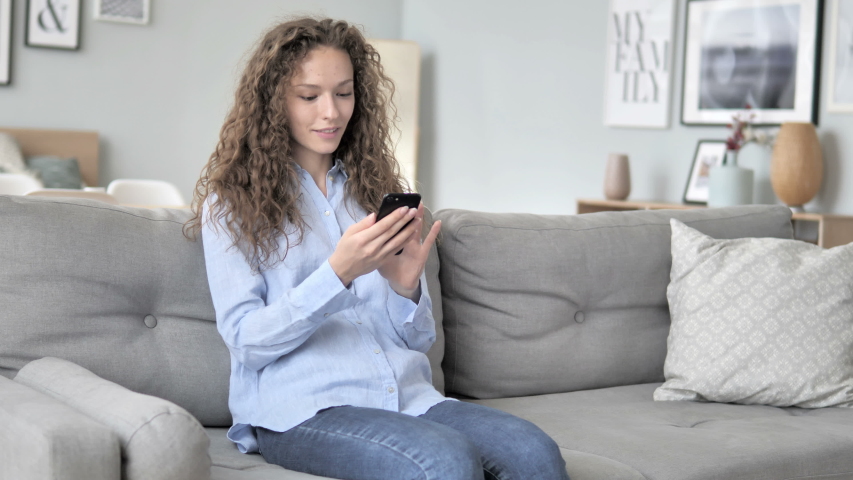Young Curly Hair Woman Using Smartphone while Relaxing on Sofa | Shutterstock HD Video #1031918471