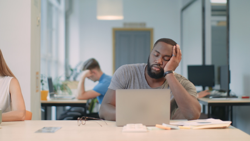 Tired man feeling sleepy at coworking space. Portrait of black man falling asleep at workplace. Boring man almost asleep at laptop computer in business office. | Shutterstock HD Video #1031923736
