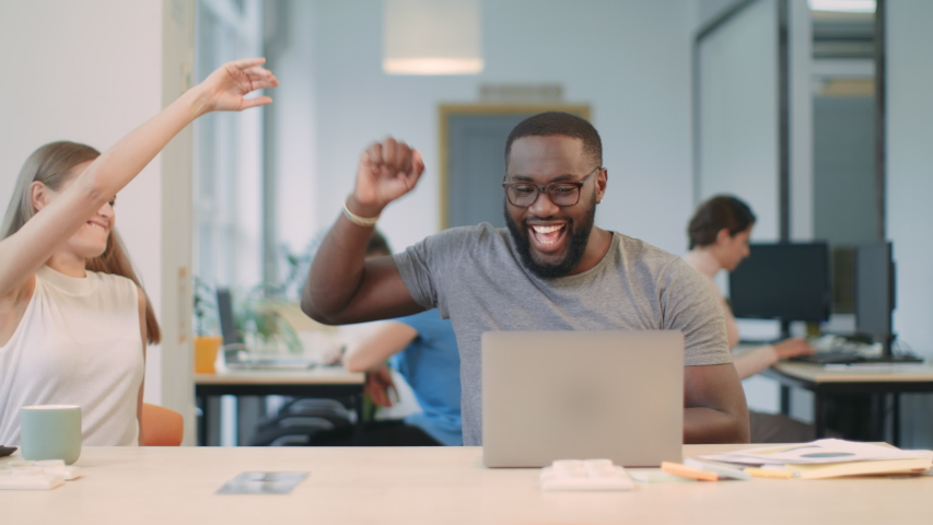 Happy african man reading good news on laptop computer at coworking space. Excited freelance man enjoy work results on notebook in open space office. Positive colleagues giving five in office. | Shutterstock HD Video #1031923745