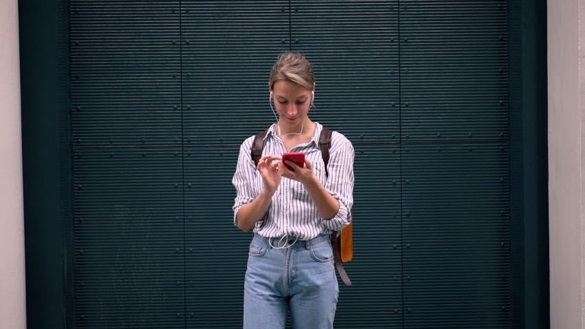 Slow motion effect of good looking female person dressed in stylish outfit enjoying favorite compositions via cool headphones, happy hipster girl for listening music and chatting vie cellular outdoors