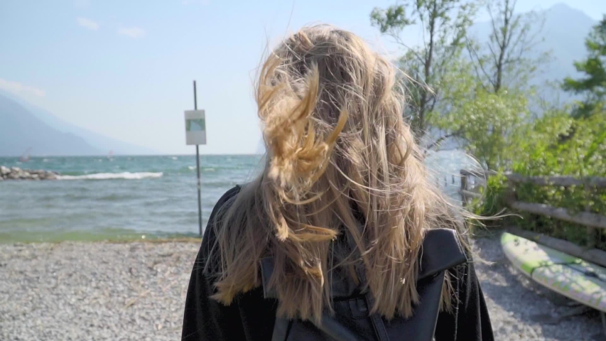 Happy smiling young blonde woman in trendy glasses posing and turning to camera,leading to the seaside.Follow me concept,positive day,good emotions.Teenage hipster girl goes hiking on a warm day.