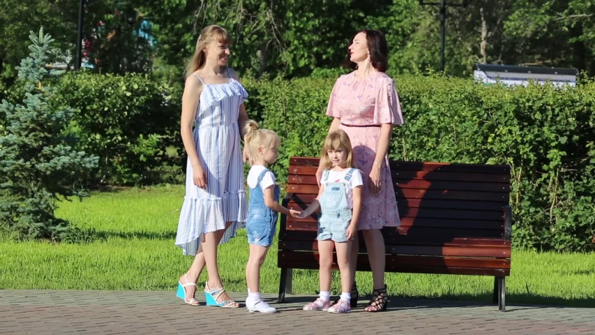 Two women with young children on the street. Women friends 35-40 years of age and small daughters 4-5 years of age are talking in the park.