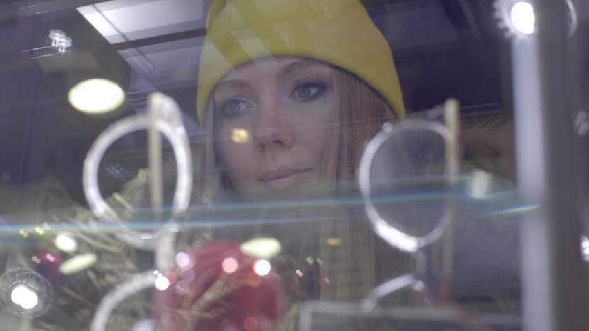 Young attractive blonde woman doing window shopping. Beautiful teenage girl standing in front of boutique,looking at store front. Christmas holidays, lifestyle, sale and retail industry concept.