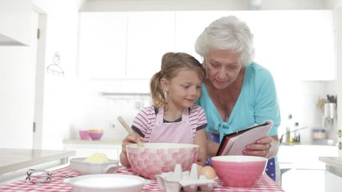 Grandmother reads recipe before showing granddaughter how to mix ingredients together which she then copies.Shot on Canon 5D Mk2 at at a frame rate of 25 fps