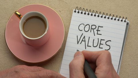 Core values - man hand writing a note with a black marker in a spiral notebook, overhead view