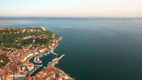 4K. Flight over old city Piran at golden sunset, aerial panoramic view with old houses, Tartini Square, St. George's Parish Church, fortress and marina.
