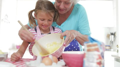 Grandmother mixes ingredients in bowl as granddaughter puts finger in and has a taste.Shot on Canon 5D Mk2 at at a frame rate of 25 fps