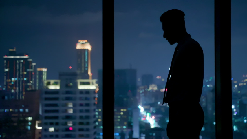Silhouette of upset businessman standing by the window at night | Shutterstock HD Video #1031954270
