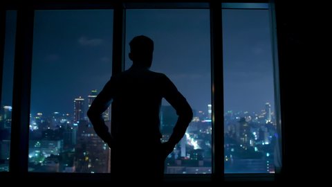 silhouette of upset businessman watching through the window at night
