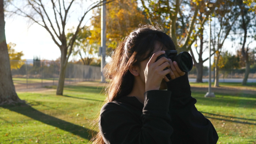 A gorgeous girl photographer taking pictures at sunset with a digital camera for photography in slow motion.