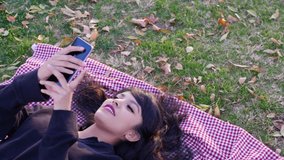 A cute girl on a video chat on her smartphone laughing and smiling in slow motion in a park at sunset with autumn leaves.