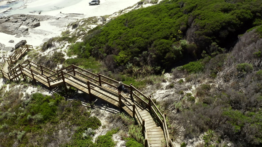 Aerial Spin Right/Forward: Walking Down Wood Steps On Grassy Hill Towards Beach - Esperance, Australia