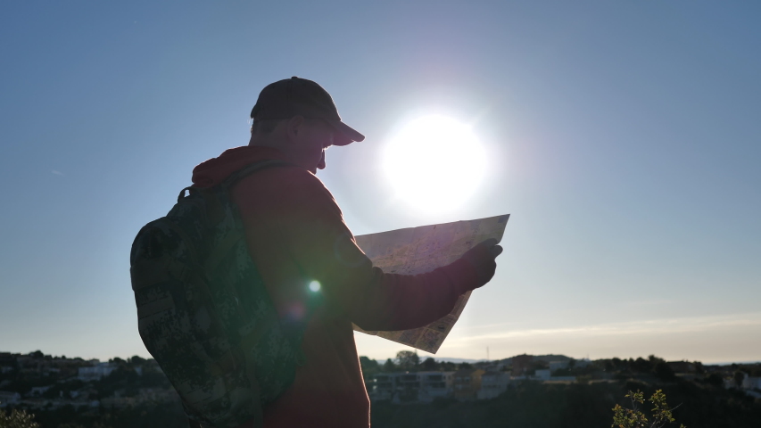 traveler man stands on top at sunrise and looks at a map