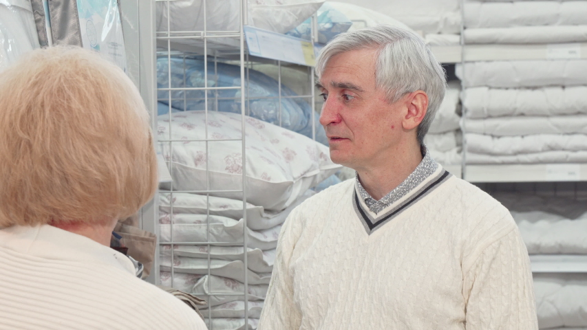 Senior man choosing bedding goods with his wife at furnishings store