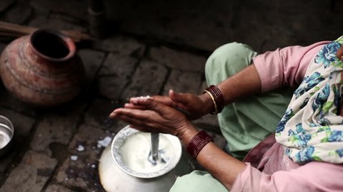 Senior women of Indian ethnicity extracting white butter from the milk in traditional style at home.