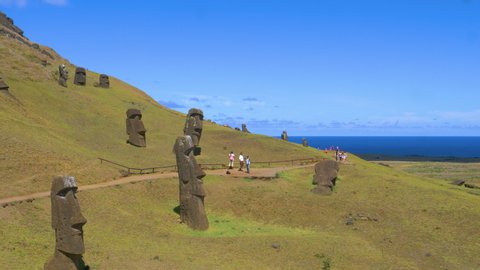 EASTER ISLAND, CHILE, MARCH 2018: AERIAL: Travelers exploring the island and observing world famous sculptures made of black volcanic matter. Tourists walking along trail and taking photos of moais.