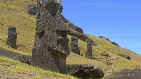 AERIAL, LOW ANGLE: Empty trail leads past a group of fascinating moai statues on sunny Easter Island. Giant megalith statues are scattered around the meadows leading up to a volcano in sunny Chile.