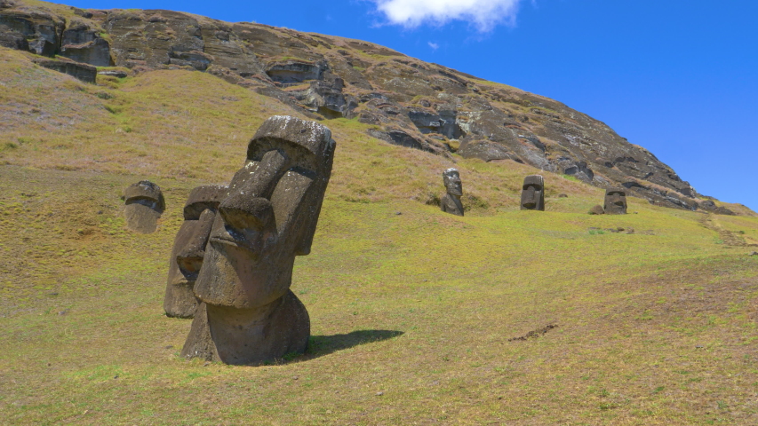 AERIAL: Ancient statues made of black volcanic rocks are scattered around the grassfields under the inactive volcano on Easter Island. Picturesque view of exotic island landscape and mysterious moais.