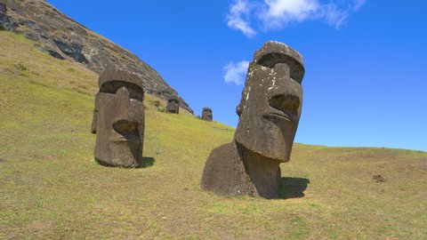 AERIAL: Ancient statues made of black volcanic rocks are scattered around the grassfields under the inactive volcano on Easter Island. Picturesque view of exotic island landscape and mysterious moais.