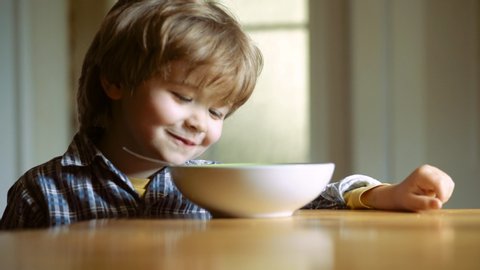 Kid eating healthy food at home. Little boy having breakfast in the kitchen. Happy baby boy spoon eats itself. Baby eating food on kitchen