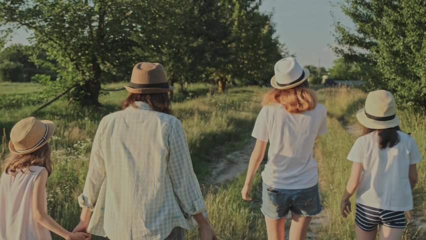 Mother walking with her daughters, woman holding the hand of child, summer natural rural landscape, golden hour
