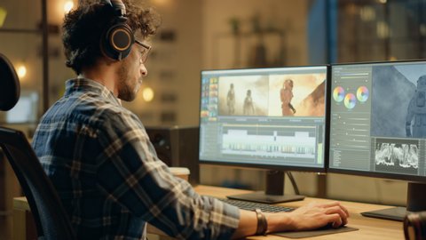 Evening in Creative Office: Professional Videographer / Audio Engineer Wearing Headphones Works on Desktop Computer, Screen Shows: Footage Montage, Using Video Editing Software, Syncing Audio Track