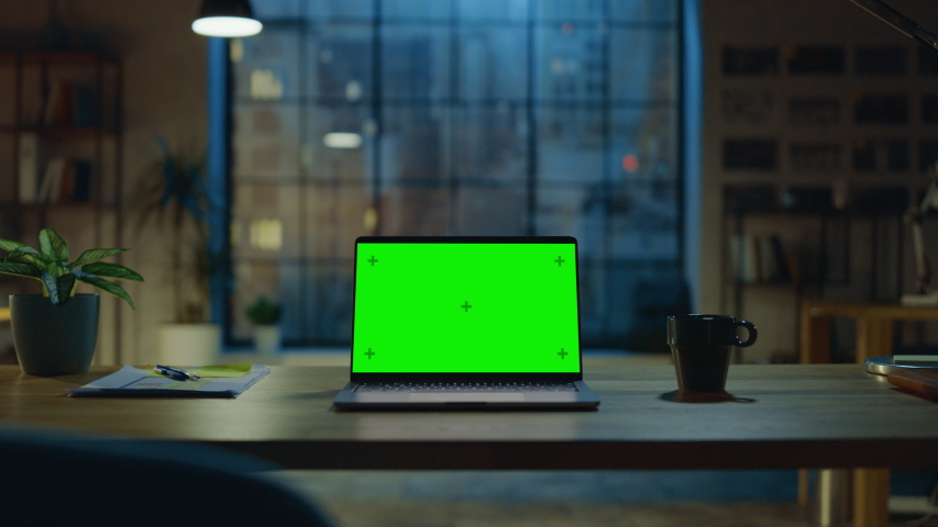 Mock-up Green Screen Laptop Standing on the Desk in the Modern Creative Office. In the Background Warm Evening Lighting and Open Space Studio with City Window View. Zoom in Shot Royalty-Free Stock Footage #1031975633