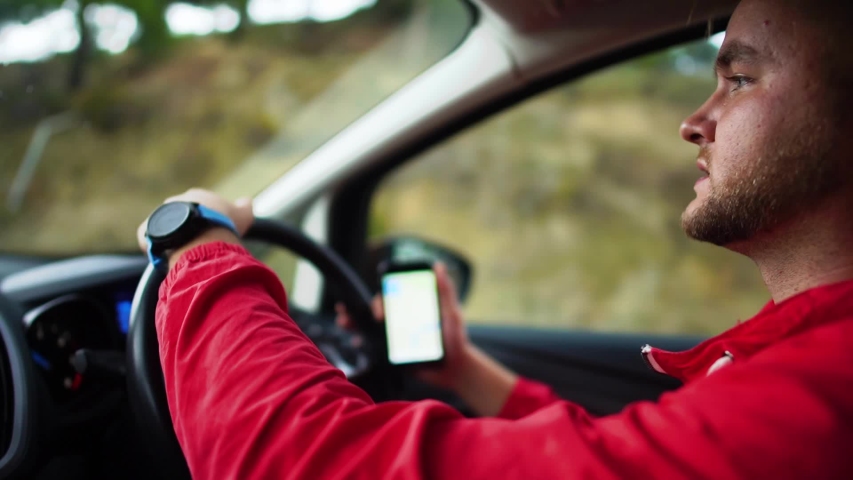 Portrait handsome bearded young man driving a car holding a cell phone with a navigation map. Cyprus. Slow motion.