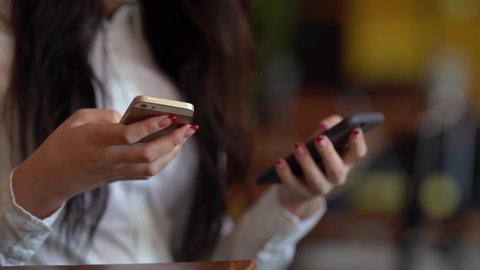 Close-up scene of girl's hands which is clicking on two phones at the same time. Woman is holding her phones in both hands and typing something from one to another.