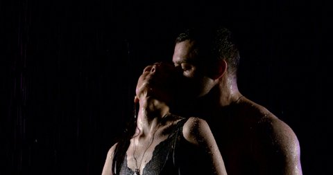 excited woman is enjoying embraces of strong muscular man under rain in darkness