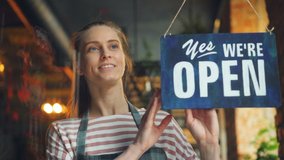 Happy cafe manager girl changing closed to open sign on window smiling looking outside waiting for clients. Small business, people and start-up concept. - Powered by Shutterstock - Get 15% off with code: PIKWIZARD15