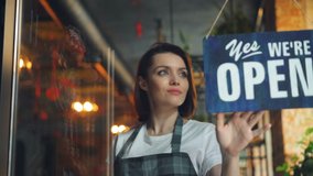 Business owner attractive woman in apron hanging we're open sign on front door smiling welcoming clients to new cafe. Business, people and youth concept. - Powered by Shutterstock - Get 15% off with code: PIKWIZARD15