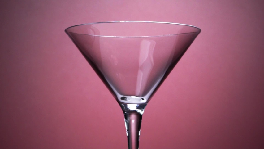 Jet Of Champagne Of Carbonated Drink Or An Alcoholic Cocktail Is Poured Into Glass Goblet On A Pink Background. Concept Of Tasting Alcoholic And Non-alcoholic Beverages In Cafes Bars And Restaurants