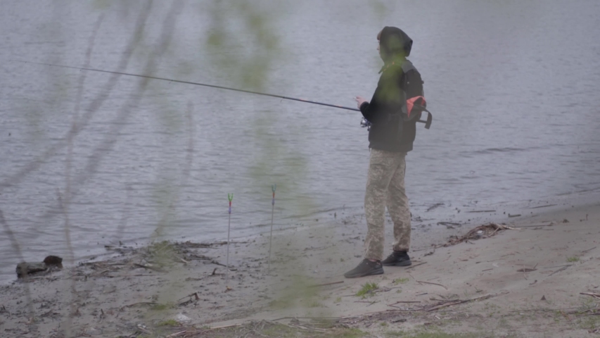 Portrait young confident fisherman in the early morning spinning fishing in river near the city. Fishing rod and a reel. Fly fisher on the river.