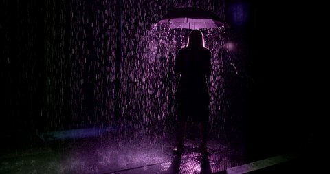 Wide shot of woman with umbrella silhouetted against purple light. Slow motion 4K recorded at 60fps