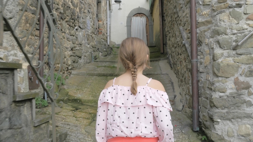 A young girl is walking through an old alley with her hands in her short pocket.