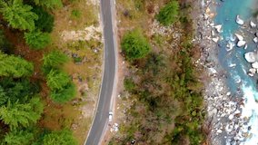 Drone video winding road in forest car moving and blue river on the side