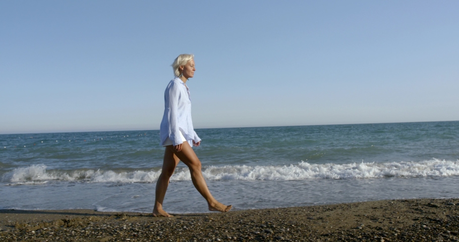 blond lady in white summer dressing walks along sandy beach